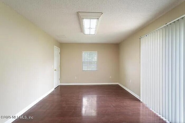 empty room with baseboards, a textured ceiling, and wood finished floors