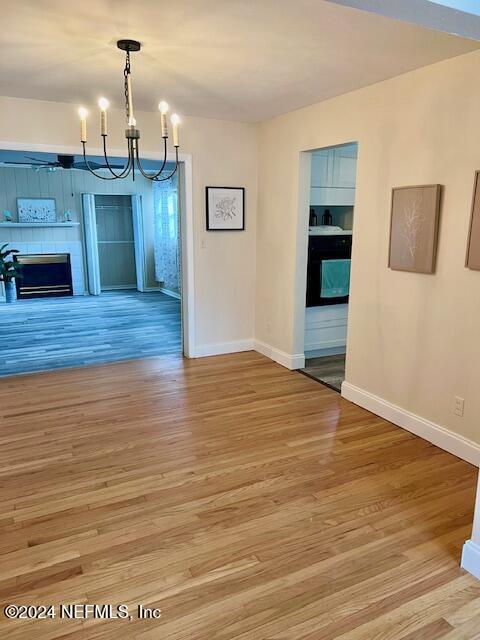 unfurnished dining area featuring a fireplace, baseboards, light wood-style floors, and an inviting chandelier