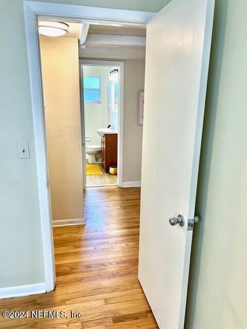 hallway with light wood-type flooring, baseboards, and a sink