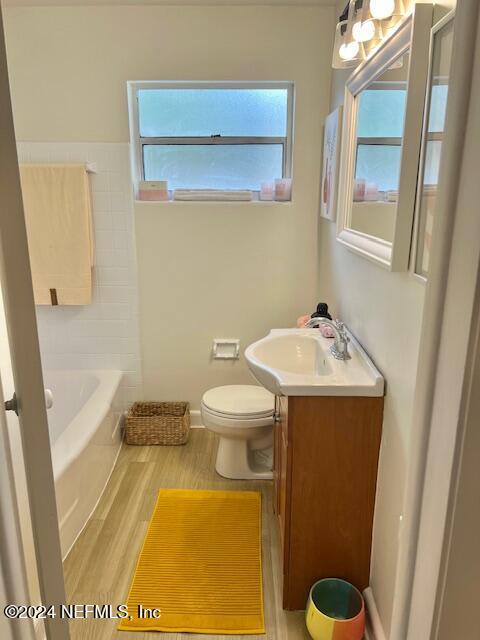 bathroom with a bath, toilet, vanity, and wood finished floors