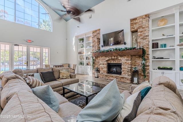 living room with built in features, a towering ceiling, a fireplace, and a ceiling fan