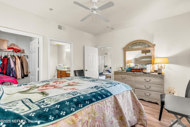 bedroom with light wood-type flooring, visible vents, a walk in closet, a ceiling fan, and a closet