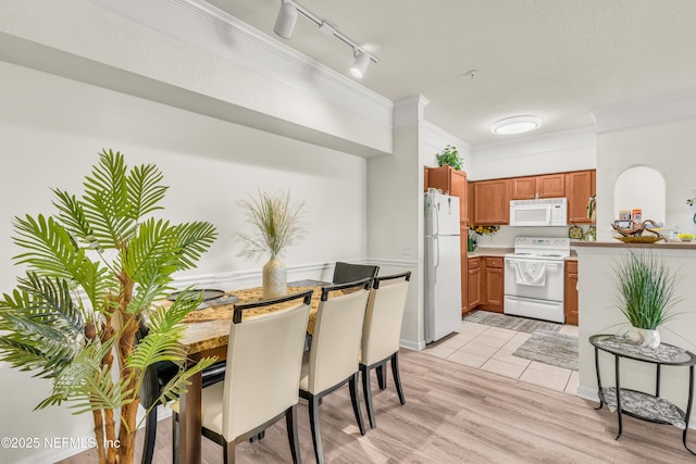 kitchen with light wood finished floors, ornamental molding, white appliances, brown cabinetry, and light countertops