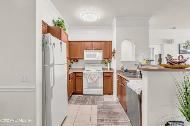 kitchen with white appliances, a peninsula, light tile patterned flooring, a sink, and brown cabinets