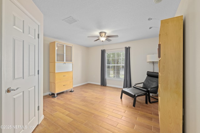 sitting room with baseboards, visible vents, ceiling fan, a textured ceiling, and light wood-type flooring