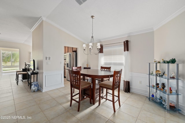 dining room featuring light tile patterned floors, an inviting chandelier, lofted ceiling, ornamental molding, and wainscoting