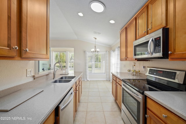 kitchen with brown cabinetry, lofted ceiling, a sink, stainless steel appliances, and a chandelier