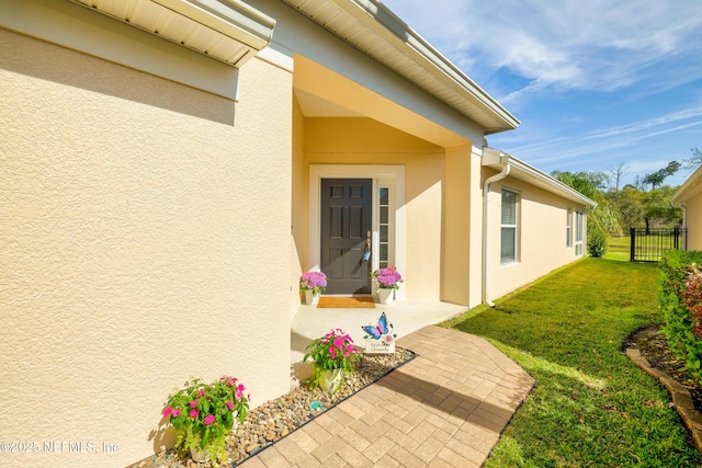 doorway to property featuring stucco siding, a yard, and fence