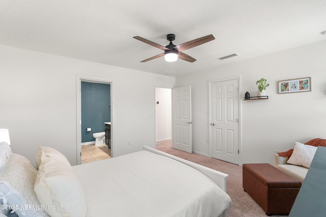 bedroom featuring visible vents, ensuite bathroom, a ceiling fan, baseboards, and light colored carpet