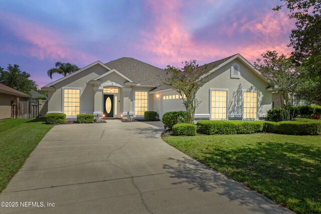 ranch-style home with stucco siding, driveway, a garage, and a front lawn