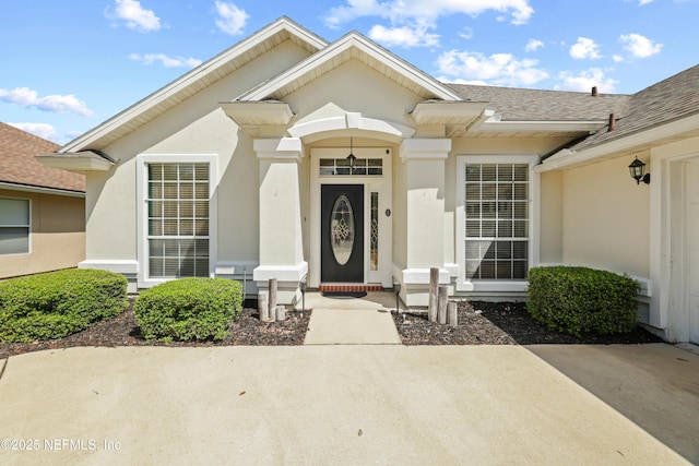 entrance to property featuring a shingled roof and stucco siding