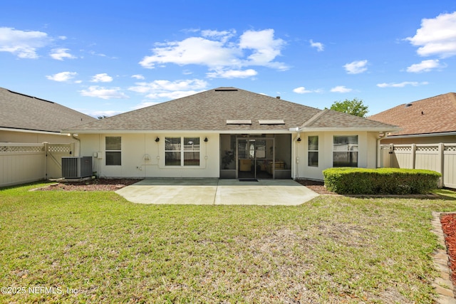 rear view of house with central air condition unit, a fenced backyard, a lawn, a patio, and roof with shingles