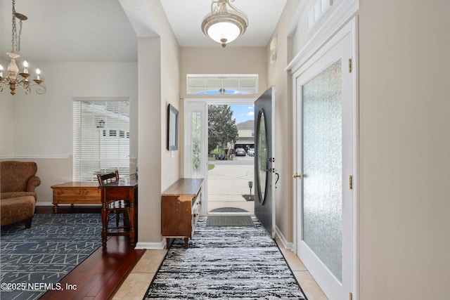 foyer featuring a chandelier, baseboards, and light tile patterned flooring