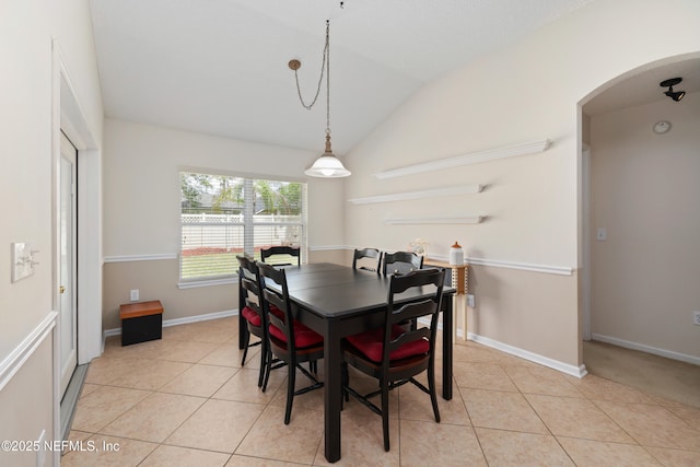dining room with baseboards, arched walkways, light tile patterned flooring, and vaulted ceiling
