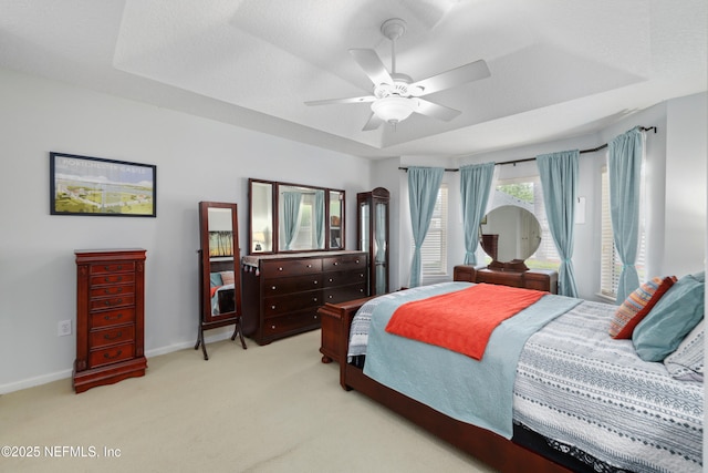bedroom with baseboards, a raised ceiling, light carpet, and a ceiling fan