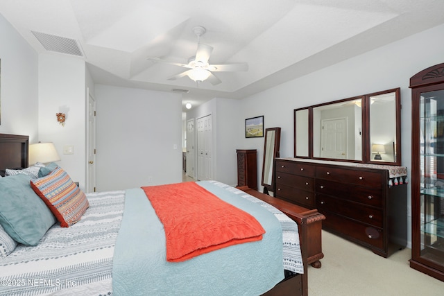bedroom with light carpet, visible vents, ceiling fan, and a raised ceiling