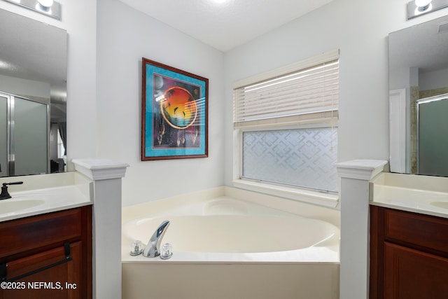 full bath featuring a sink, two vanities, a stall shower, and a garden tub