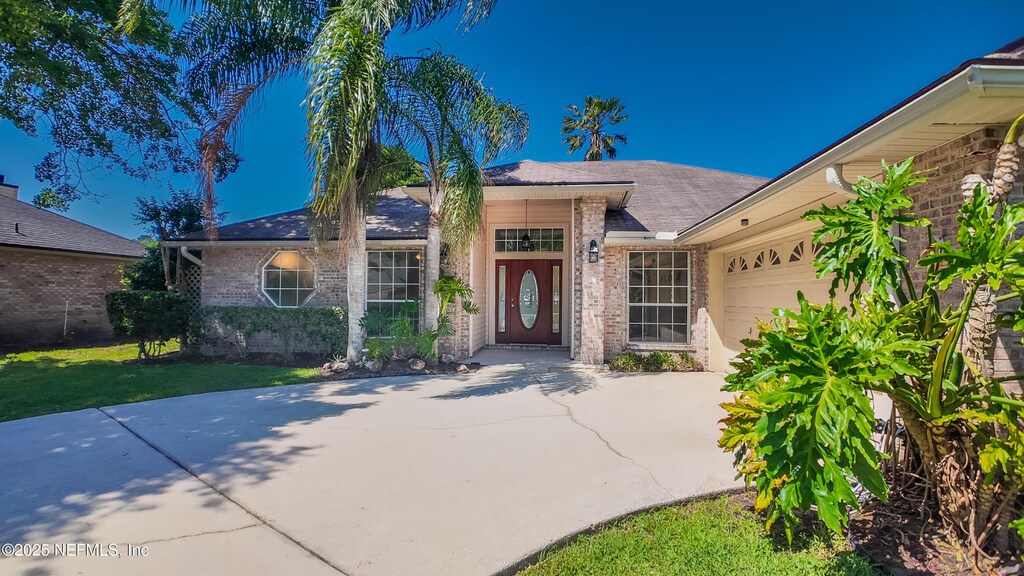 13775 Danforth Dr S, Jacksonville, FL 32224 - view of exterior entry with a garage, brick siding, concrete driveway, and a lawn
