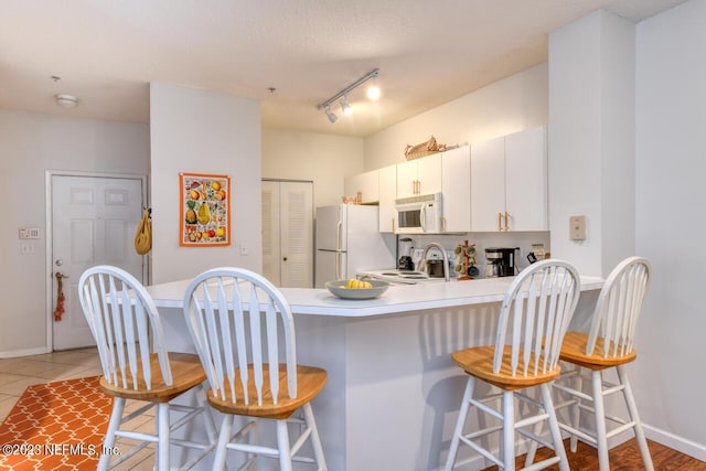 kitchen featuring baseboards, a breakfast bar area, light countertops, a peninsula, and white appliances