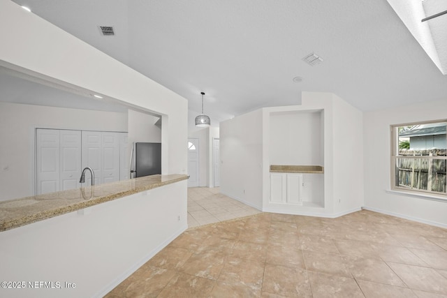 unfurnished living room featuring visible vents, a sink, light tile patterned floors, and vaulted ceiling