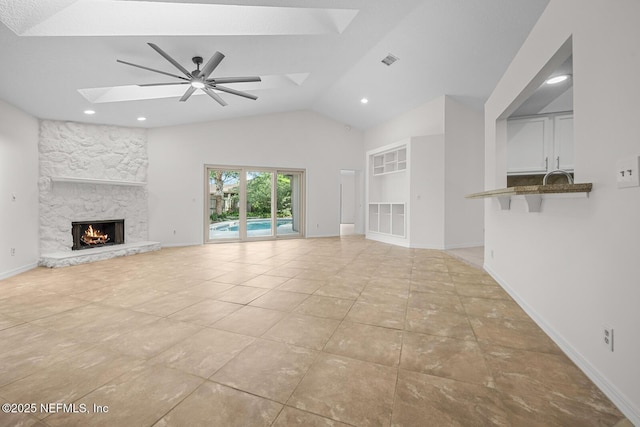 unfurnished living room featuring ceiling fan, visible vents, a skylight, a fireplace, and light tile patterned floors
