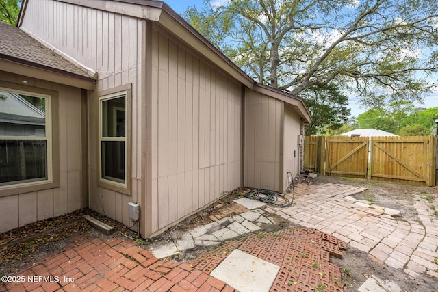 view of side of home with a patio, fence, a gate, and roof with shingles
