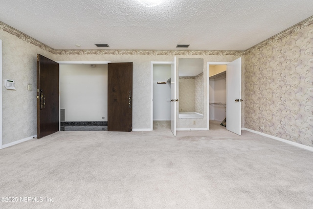 unfurnished bedroom featuring visible vents, carpet flooring, a textured ceiling, and wallpapered walls