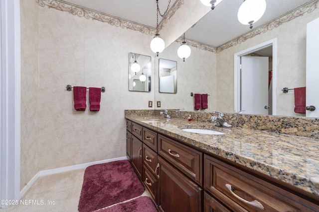 full bath with double vanity, a textured ceiling, baseboards, and a sink