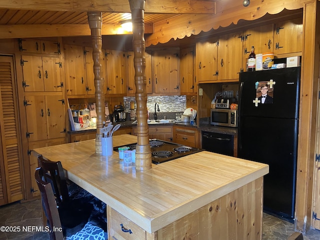 kitchen featuring stone finish floor, black appliances, beam ceiling, and butcher block countertops