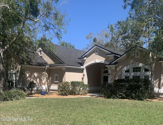 view of front facade featuring a front lawn, stucco siding, and roof with shingles