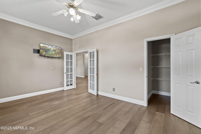 unfurnished bedroom with french doors, wood finished floors, a walk in closet, visible vents, and ornamental molding