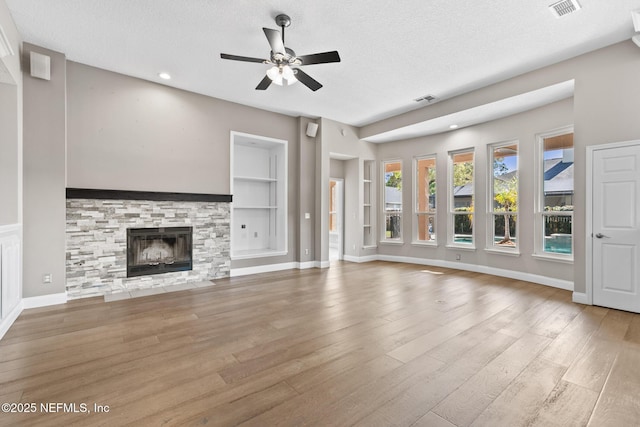unfurnished living room featuring a textured ceiling, visible vents, wood finished floors, and built in shelves
