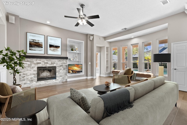 living room featuring a textured ceiling, visible vents, a fireplace, wood finished floors, and built in shelves