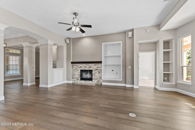 unfurnished living room with ceiling fan, built in shelves, decorative columns, and wood finished floors