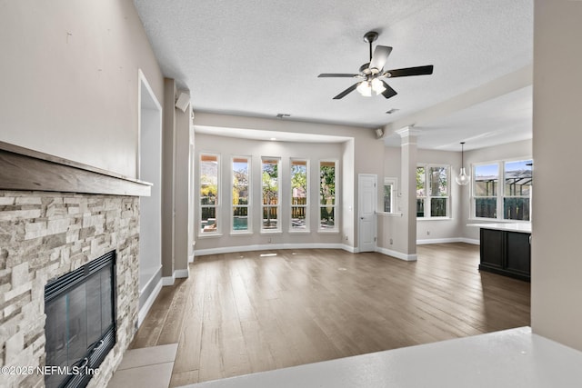 unfurnished living room featuring a stone fireplace, a textured ceiling, a ceiling fan, and hardwood / wood-style flooring
