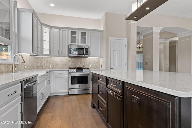 kitchen featuring dark wood-style flooring, ornate columns, light stone countertops, stainless steel appliances, and white cabinetry