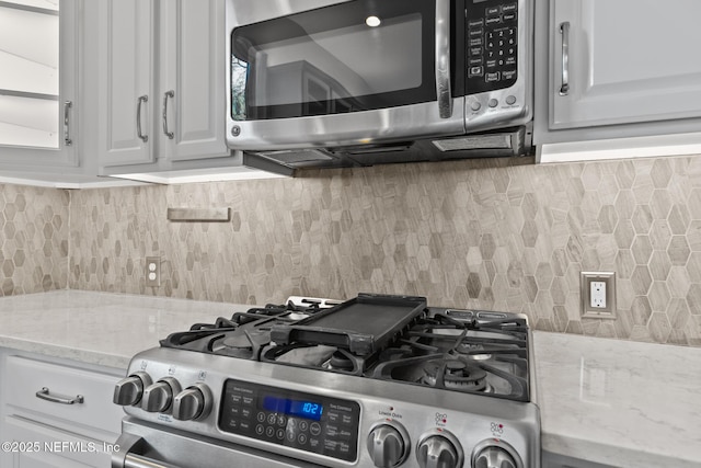 room details featuring tasteful backsplash, light stone countertops, appliances with stainless steel finishes, and white cabinets