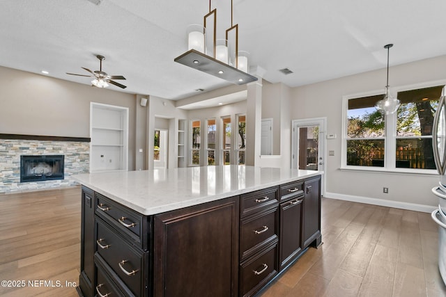 kitchen featuring a ceiling fan, wood finished floors, open floor plan, baseboards, and decorative light fixtures