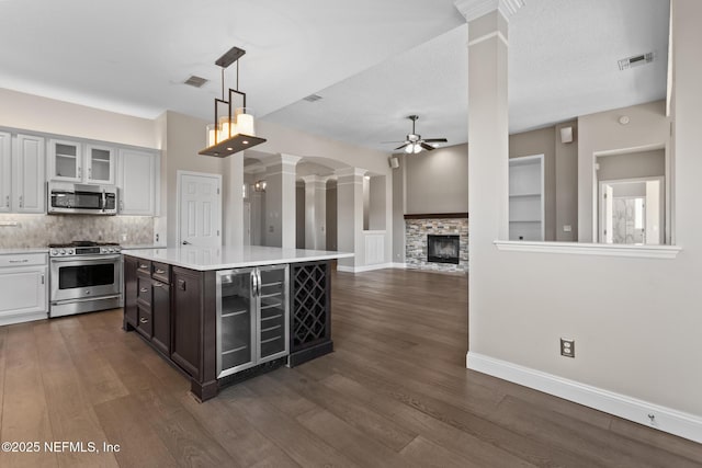 kitchen featuring appliances with stainless steel finishes, beverage cooler, visible vents, ceiling fan, and ornate columns