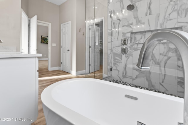 full bathroom featuring a freestanding tub, a marble finish shower, baseboards, and wood finished floors