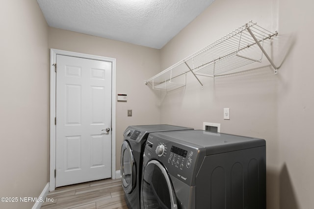 laundry room featuring washing machine and clothes dryer, a textured ceiling, baseboards, laundry area, and light wood-type flooring