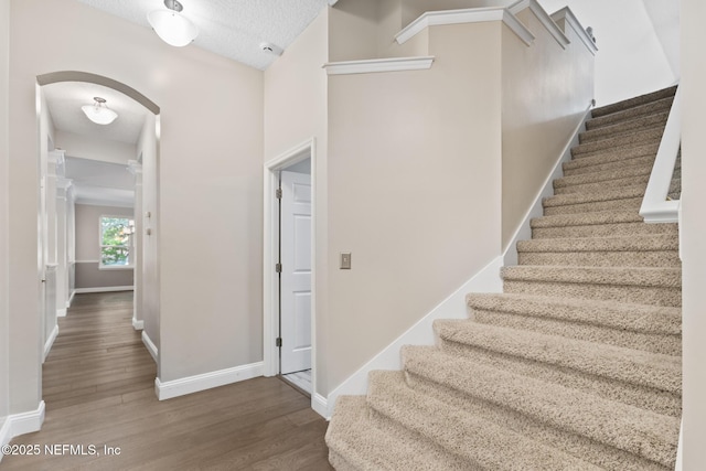 staircase with baseboards, wood finished floors, arched walkways, and a textured ceiling