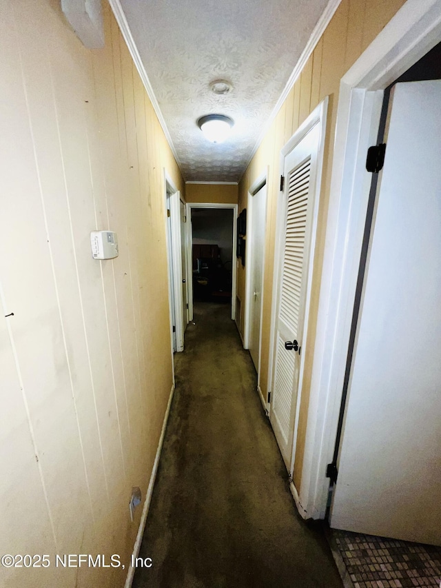 hallway with wooden walls, a textured ceiling, and crown molding