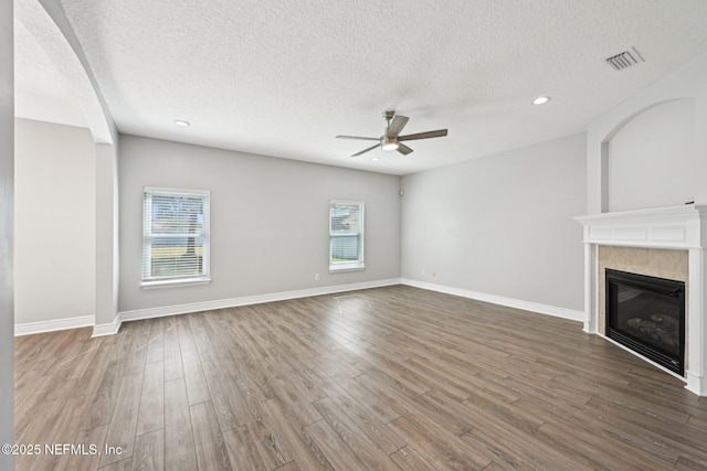 unfurnished living room featuring visible vents, wood finished floors, ceiling fan, and a fireplace