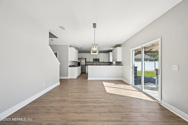kitchen with baseboards, open floor plan, stainless steel appliances, wood finished floors, and white cabinetry