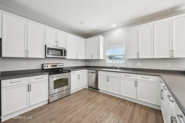 kitchen featuring dark countertops, a textured ceiling, stainless steel appliances, light wood-style floors, and white cabinets