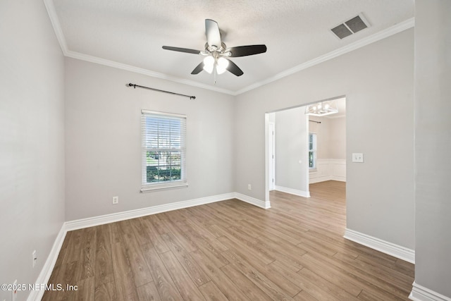 empty room with visible vents, wood finished floors, ornamental molding, and ceiling fan with notable chandelier