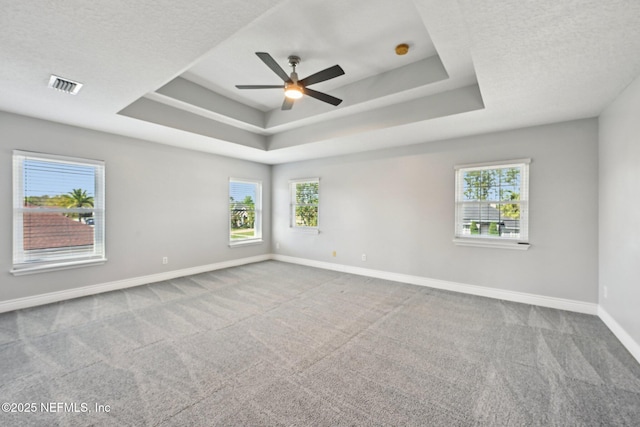carpeted spare room featuring visible vents, a ceiling fan, a tray ceiling, a textured ceiling, and baseboards