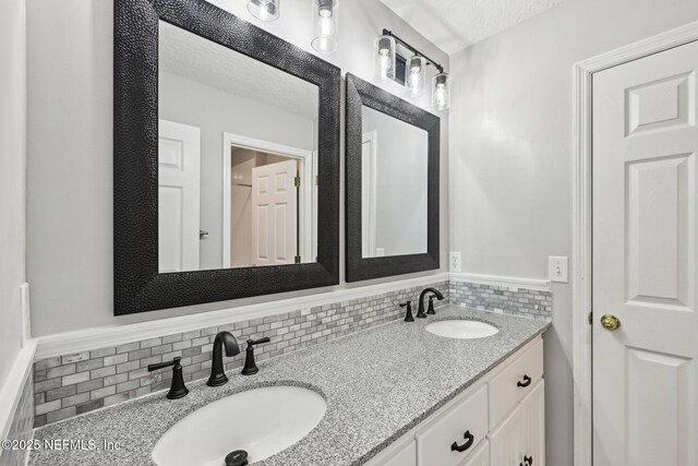 full bath featuring double vanity, decorative backsplash, a textured ceiling, and a sink