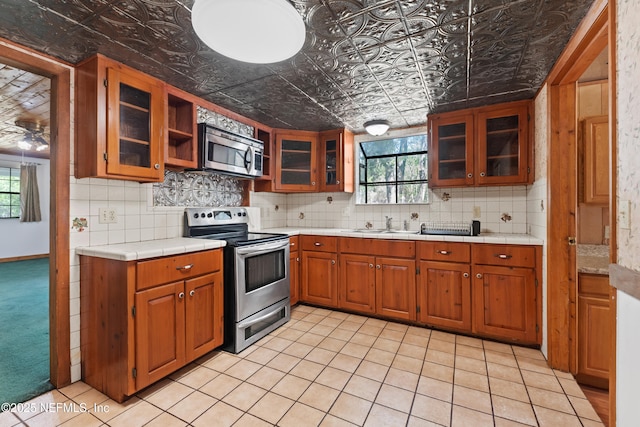 kitchen featuring decorative backsplash, appliances with stainless steel finishes, brown cabinets, and an ornate ceiling